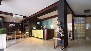 A hotel lobby with a reception desk, seating area, and a decorative flower arrangement. - MP Hotel Kelapa Gading (Jakarta)