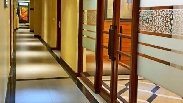 A long, well-lit hallway with a tiled floor, wooden doors, and a patterned wall design. - MP Hotel Kelapa Gading (Jakarta)