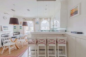Une cuisine lumineuse avec des meubles blancs, un coin repas avec des chaises blanches et une grande fenêtre qui laisse entrer la lumière naturelle.