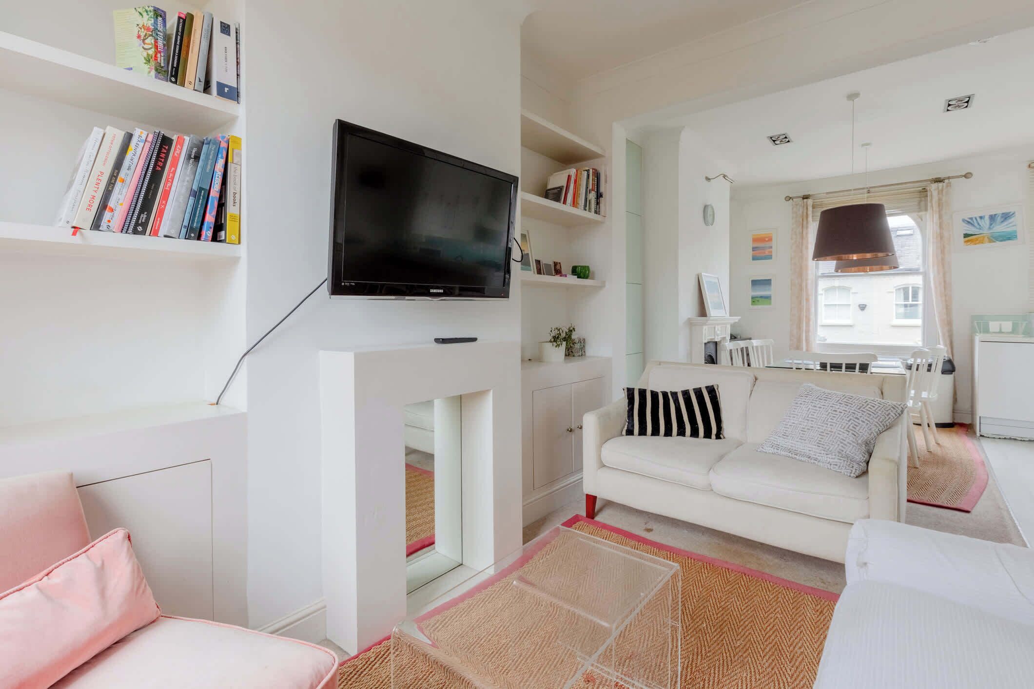 A living room with a flat-screen TV, white sofas, a bookshelf, and a fireplace.