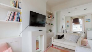 Una sala de estar con televisor de pantalla plana, sofás blancos, una estantería y una chimenea.