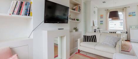 A living room with a flat-screen TV, white sofas, a bookshelf, and a fireplace.