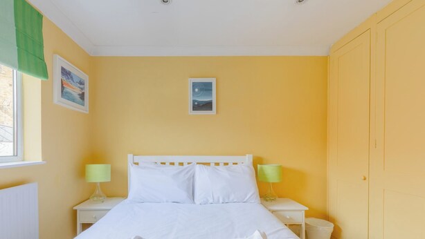 Un dormitorio con una cama, dos mesitas de noche, dos lámparas, una ventana con cortinas y una puerta.