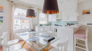 Una cocina moderna con armarios blancos, una mesa de comedor de vidrio y lámparas colgantes.