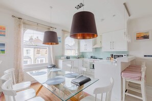 A modern kitchen with white cabinets, a glass dining table, and pendant lights.