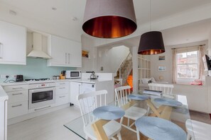 Une cuisine moderne avec des meubles blancs, une cuisinière en acier inoxydable et une table à manger en verre, assortie de chaises blanches.