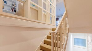 Una escalera con barandilla blanca, una puerta con ventanal y una estantería llena de libros.