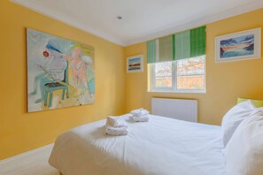 Une chambre d’hôtel avec un lit, un tableau au mur, une fenêtre donnant sur un paysage et un radiateur.