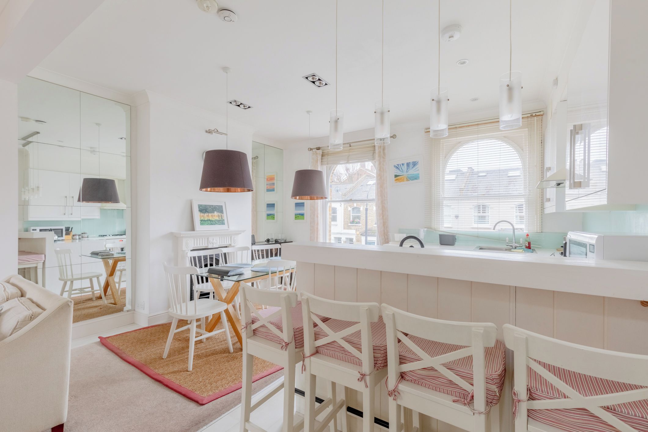Une cuisine moderne avec des meubles blancs, un îlot central et des luminaires suspendus.