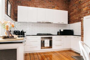 A modern kitchen with white cabinets, a brick wall, and a wooden floor.