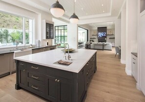 A spacious kitchen with a large island, dark cabinetry, and pendant lighting. - Mandeville Canyon - Exquisite Contemporary Farmhouse with Pool & Spa (Los Angeles)