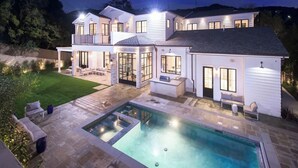 A two-story house with a swimming pool, outdoor seating, and a well-lit patio area.
