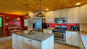 A kitchen with white cabinets, a granite countertop, stainless steel appliances, and a wooden ceiling. - Fairview Lodge on 4th Lake (Old Forge)