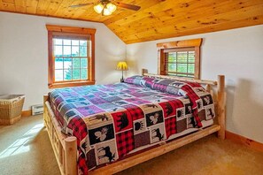 A bedroom with a wooden bed, two windows, a ceiling fan, and a lamp. - Fairview Lodge on 4th Lake (Old Forge)