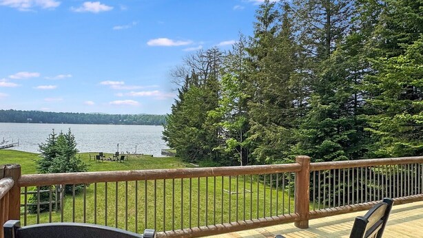 A wooden deck with a view of a lake and forest. - Fairview Lodge on 4th Lake (Old Forge)