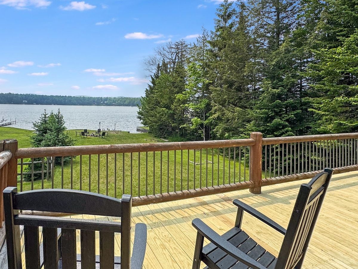A wooden deck with a railing overlooking a lake, surrounded by trees.