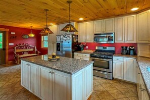 A kitchen with a central island, stainless steel appliances, and white cabinetry. - Fairview Lodge on 4th Lake (Old Forge)