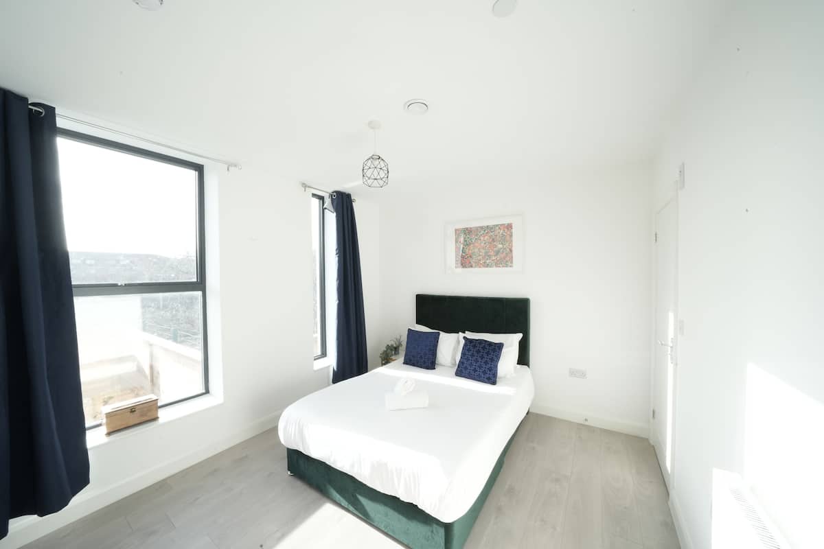 A modern bedroom with a large window, a bed with white bedding, and a green headboard.