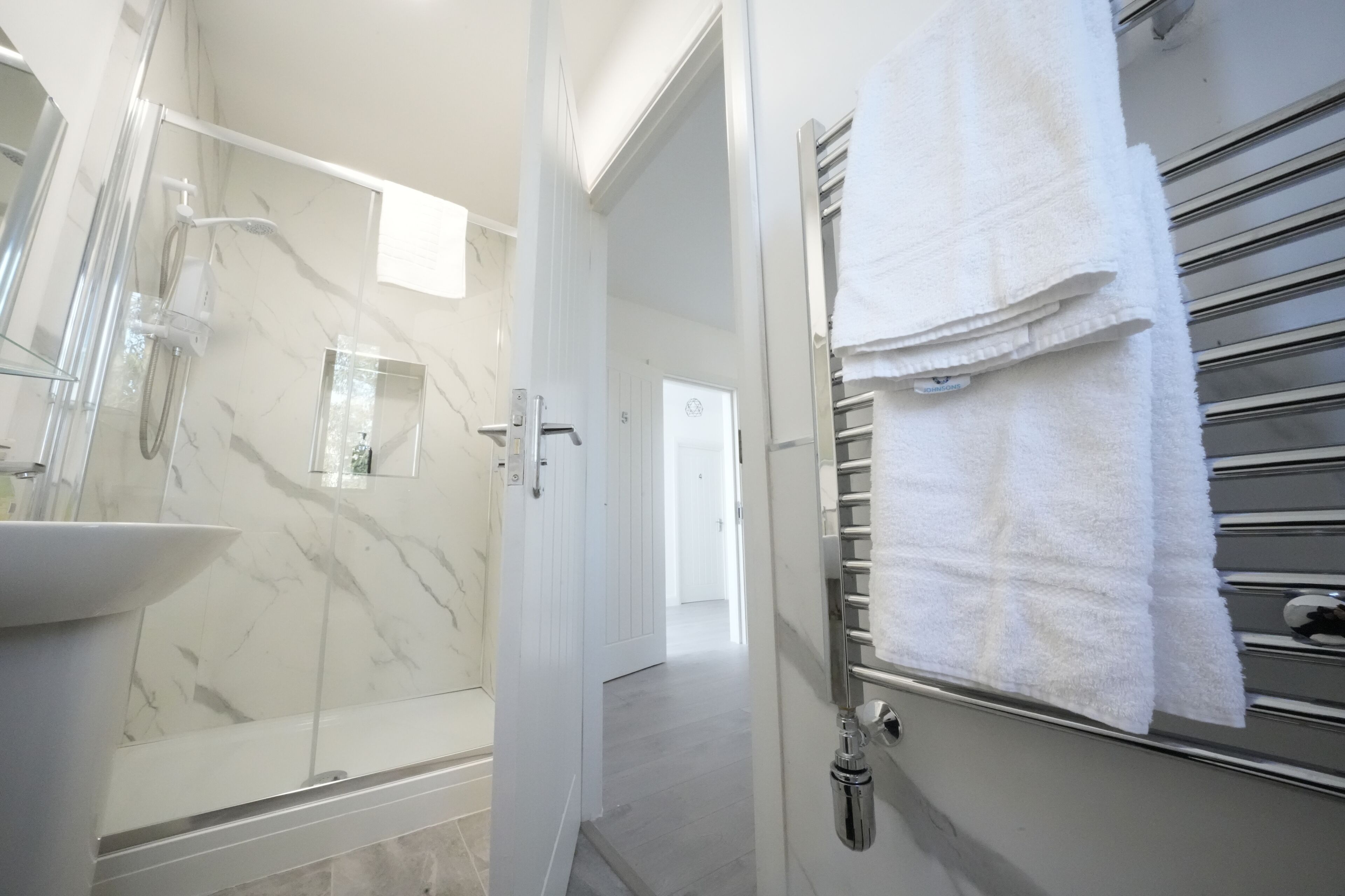 A modern bathroom with a glass-enclosed shower, a white sink, and a towel rack with folded towels.