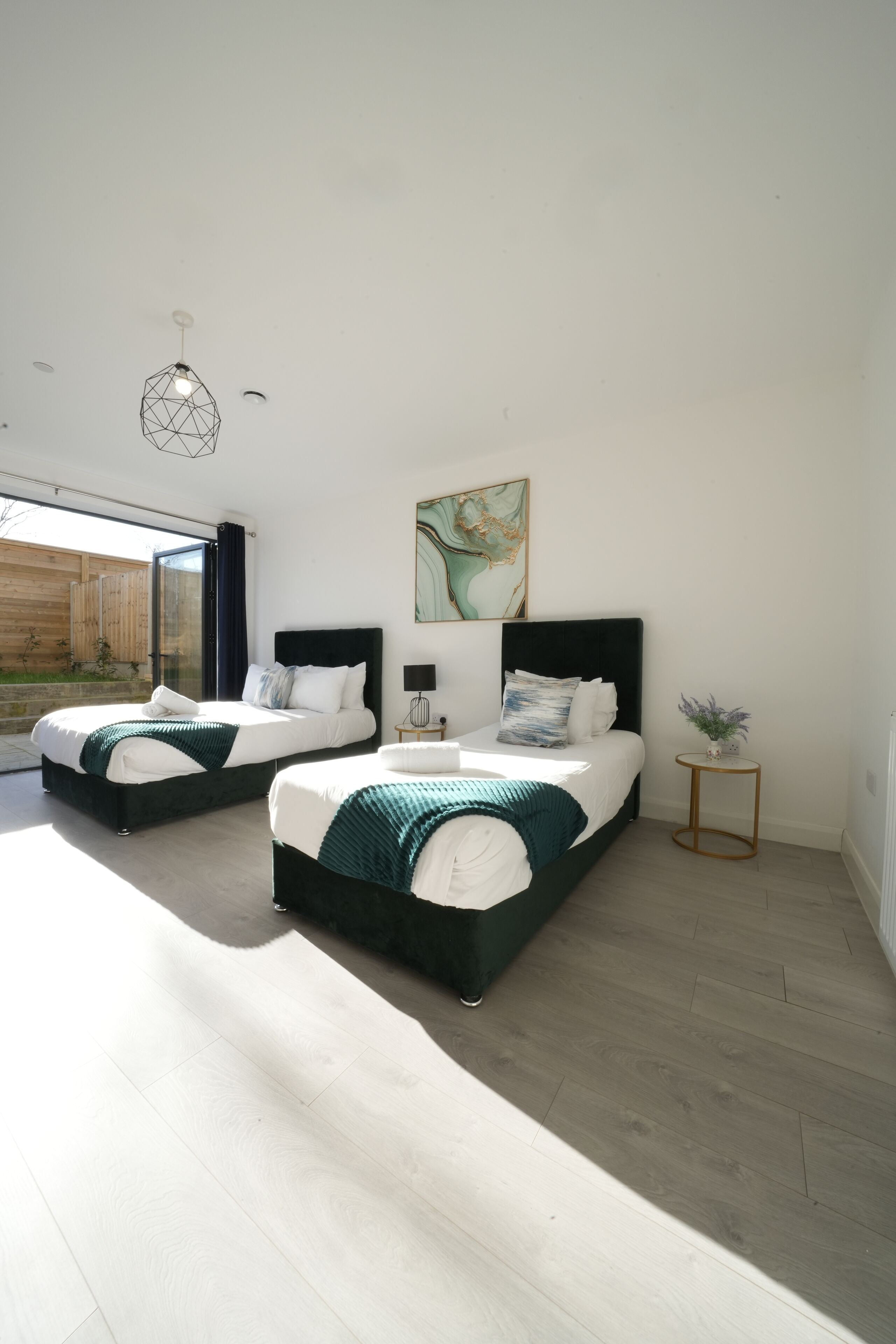 Une chambre moderne avec deux lits, une grande fenêtre et une petite table de chevet.