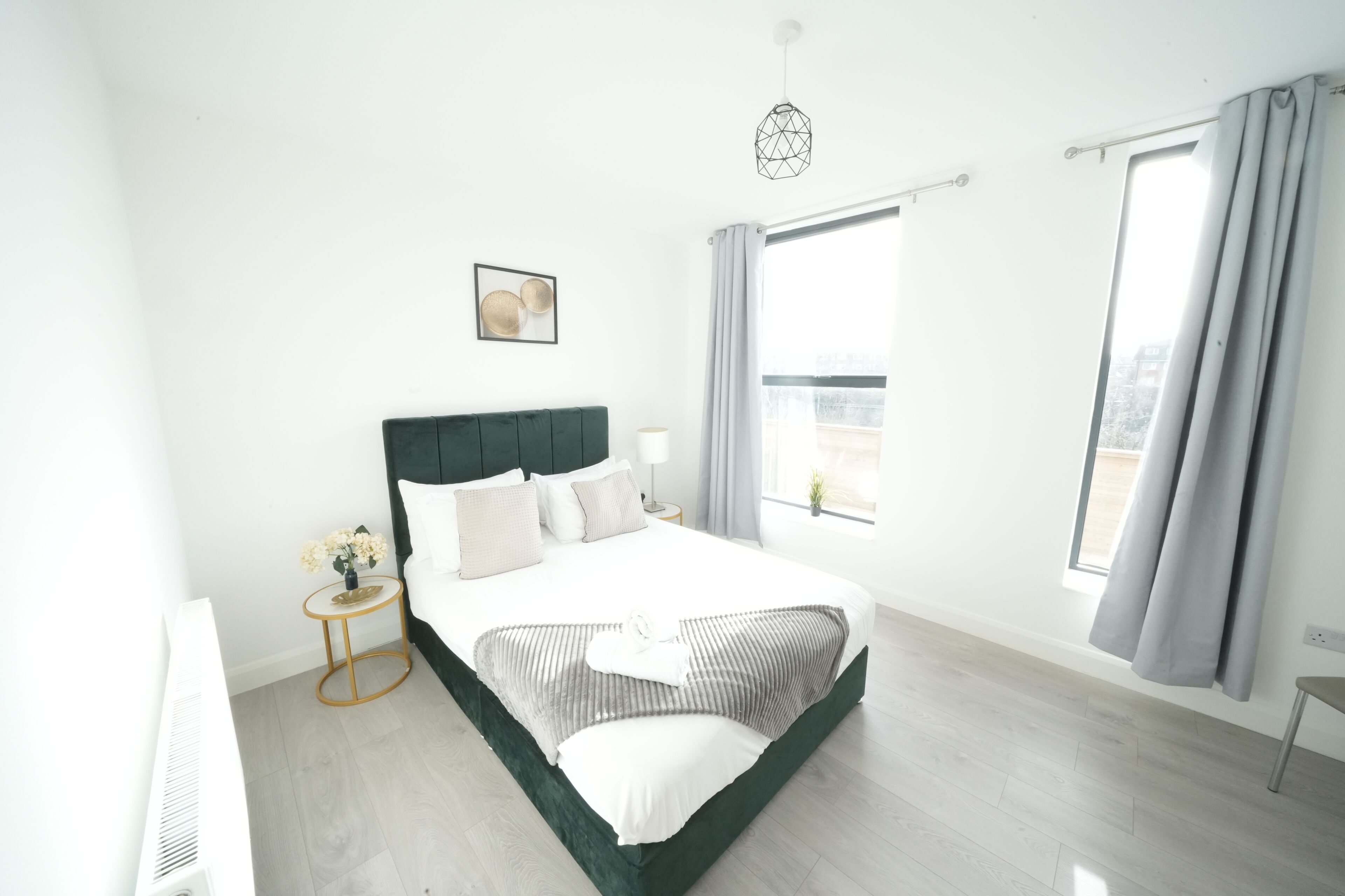 Un dormitorio moderno con una cama grande, una mesita de noche, una lámpara colgante y un ventanal con cortinas.