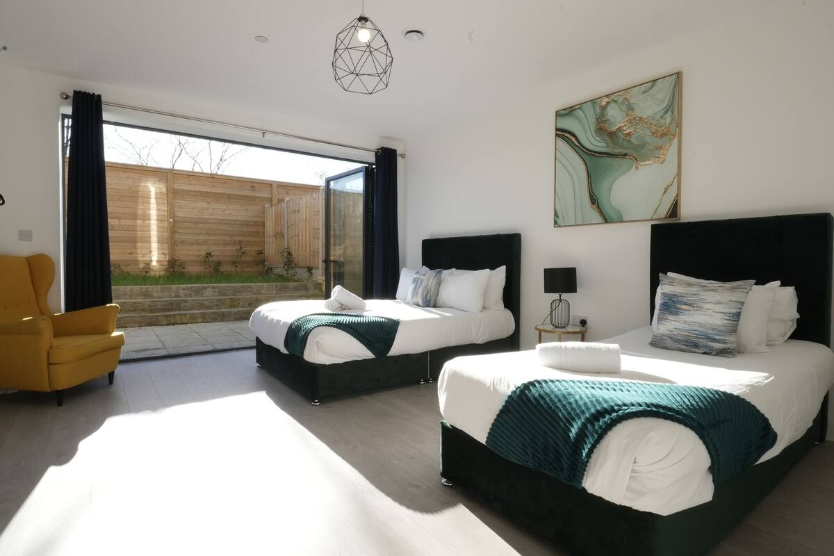 A modern bedroom with two beds, a yellow armchair, and a large window.