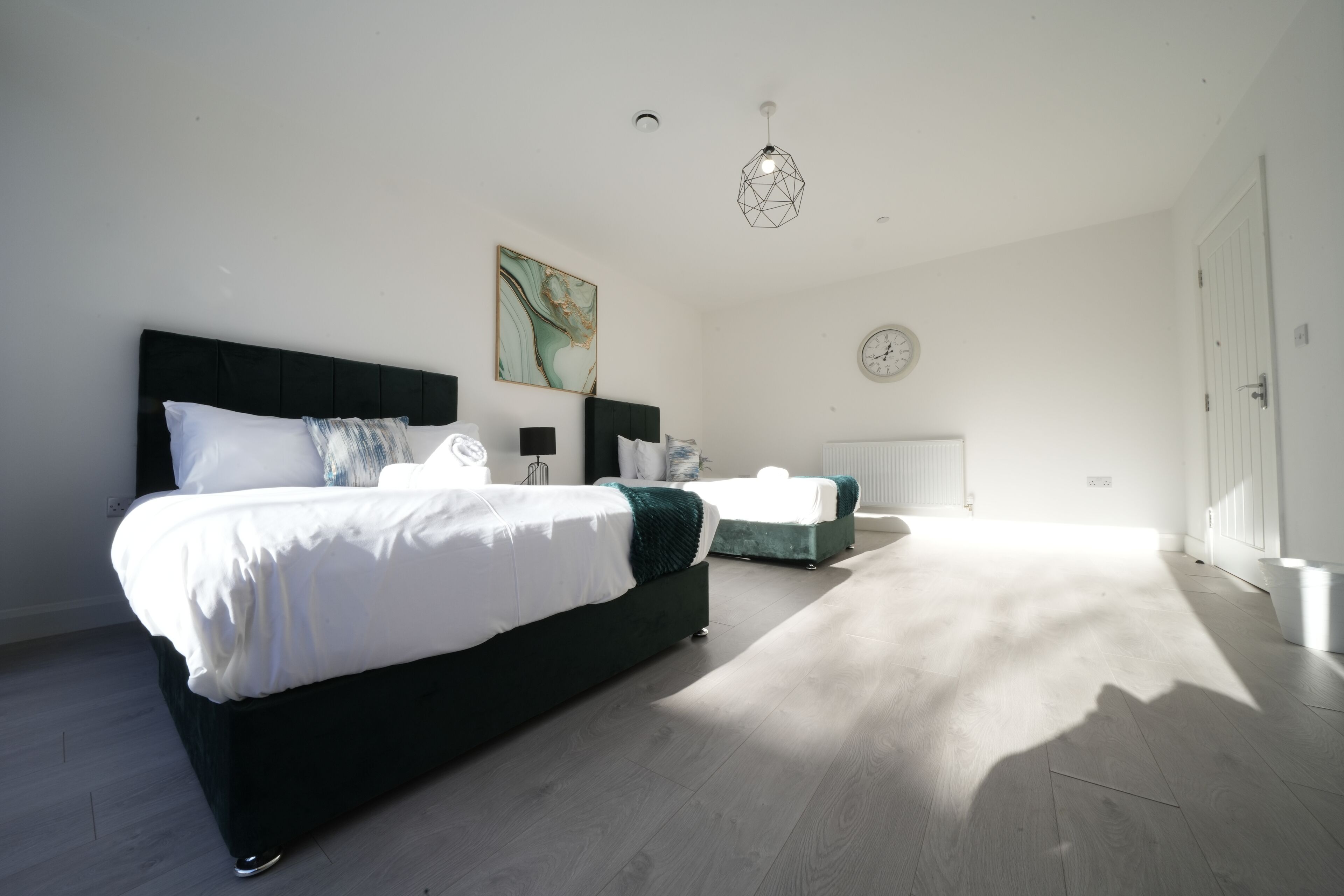 A bedroom with a large bed, a smaller bed, a nightstand, a wall clock, and a geometric pendant light.