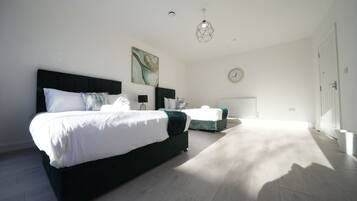 A bedroom with a large bed, a smaller bed, a nightstand, a wall clock, and a geometric pendant light.
