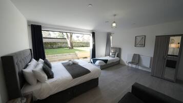 A modern bedroom with a large bed, a smaller bed, a sofa, a chair, and a view of the garden.