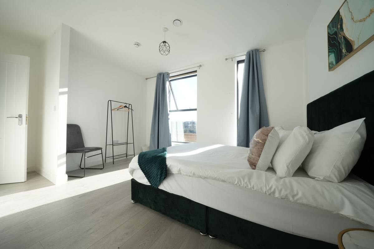 A modern bedroom with a large bed, a chair, a wardrobe, and a window with curtains.
