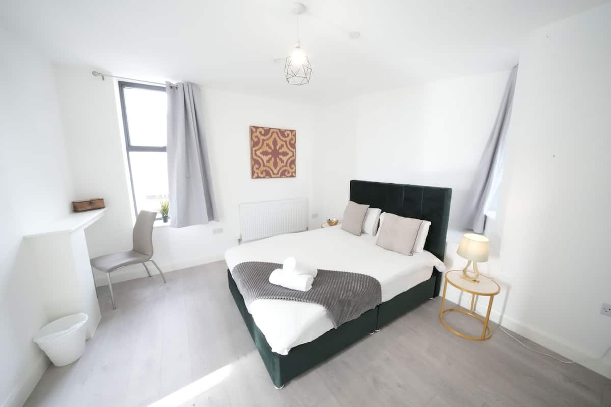 A modern bedroom with a large bed, a bedside table, a chair, and a window with curtains.