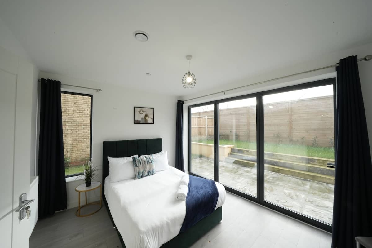 A modern bedroom with a large window, a bed with white bedding, a small bedside table, and a hanging light fixture.