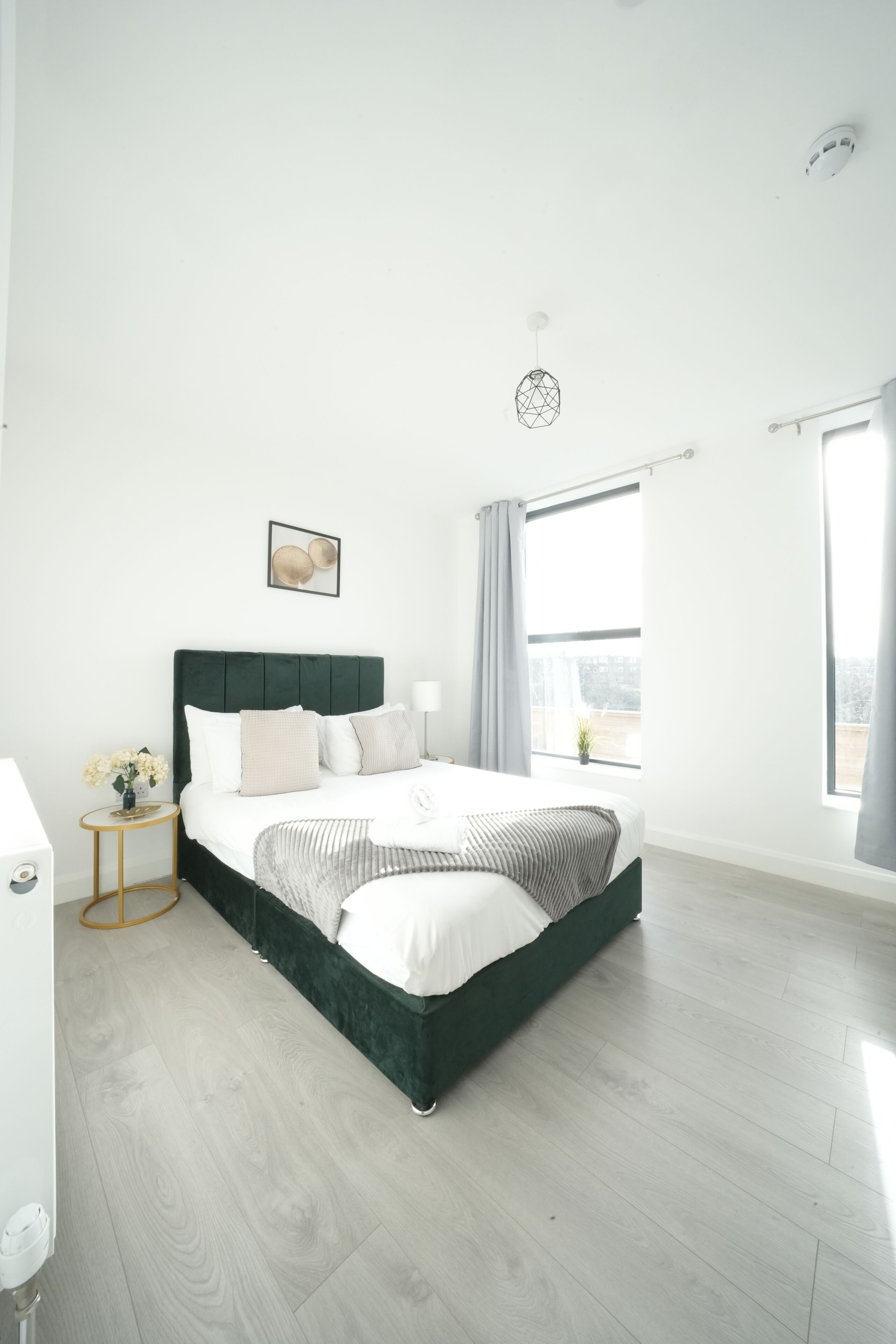 Een moderne slaapkamer met een groot bed, een nachtkastje, een klein rond tafeltje en een raam met gordijnen.
