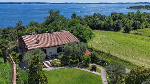 Une maison avec un toit recouvert de tuiles rouges, entourée d’une végétation luxuriante et offrant une vue sur une vaste étendue d’eau.