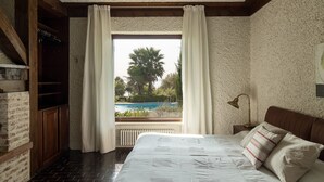 Une chambre avec un grand lit, une vue sur une piscine et un mur en briques.