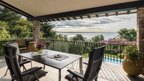 Une terrasse extérieure couverte, avec une table et des chaises, une vue sur la mer et une piscine.