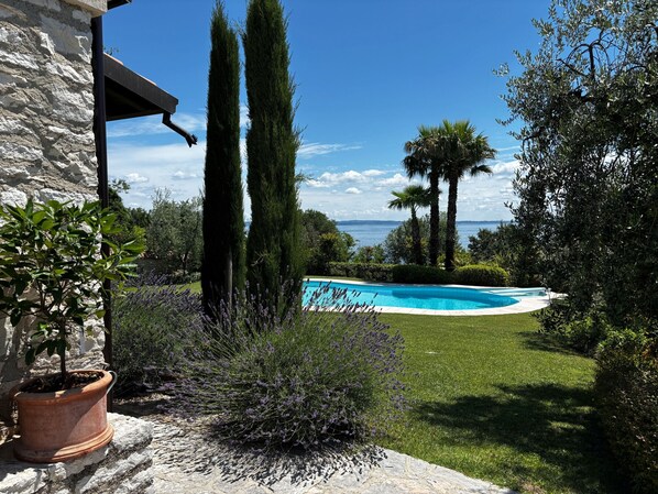 A swimming pool surrounded by greenery and a stone building.