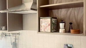 A kitchen with a gas stove, hanging utensils, and a shelf with boxes and kitchenware.