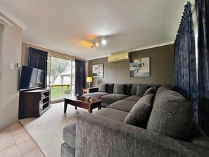 Una sala de estar con sofá, mesa de centro, televisor y ventana con cortinas.
