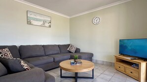 Un salon moderne avec un canapé gris, une table basse ronde en bois, un téléviseur posé sur un meuble en bois et une horloge au mur.