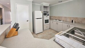 A compact kitchen with a refrigerator, microwave, oven, and sink. - Pelican Shore Villa 22 - Kalbarri WA (Kalbarri)