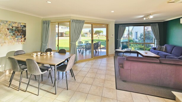 A dining area with a table and chairs, a sofa, and a view of the outdoors. - Pelican Shore Villa 22 - Kalbarri WA (Kalbarri)