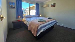 A bedroom with a bed, a ceiling fan, a nightstand, a window with curtains, and a wall-mounted air conditioner. - Pelican Shore Villa 22 - Kalbarri WA (Kalbarri)