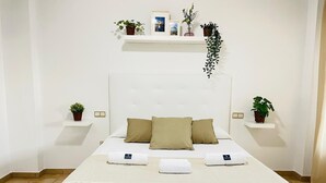 A neatly arranged bedroom with a large bed, two bedside tables, and a wall-mounted shelf with plants. - La Almadraba, Chiclana de la Frontera (Chiclana de la Frontera)