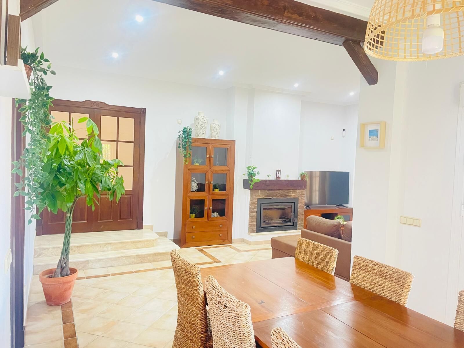 A spacious living area with a fireplace, a wooden cabinet, and a dining table with wicker chairs.