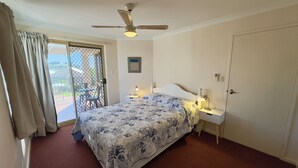 A bedroom with a bed, a ceiling fan, a nightstand, a desk, and a sliding glass door leading to an outdoor area. - Pelican Shore Villa 14 - Kalbarri WA (Kalbarri)