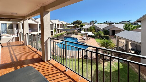 A balcony with a view of a swimming pool, a grassy area, and multiple buildings in the background. - Pelican Shore Villa 14 - Kalbarri WA (Kalbarri)