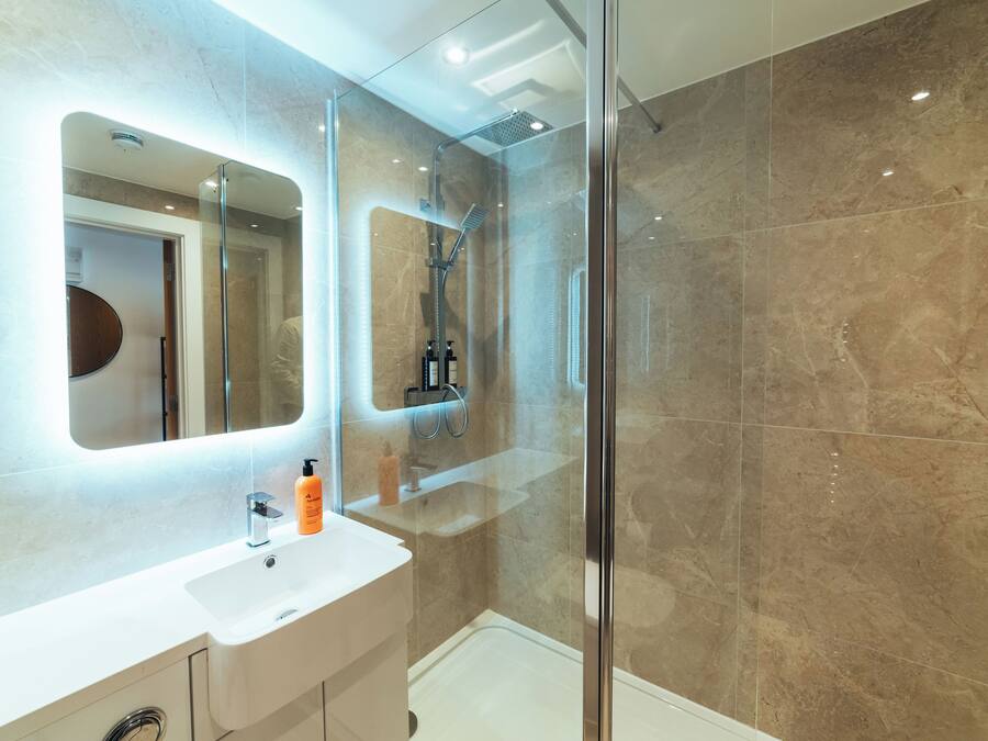Un baño moderno con ducha de vidrio, tocador blanco y un espejo grande.