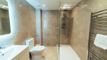 Un baño moderno con ducha acristalada, inodoro blanco y lavamanos empotrado.