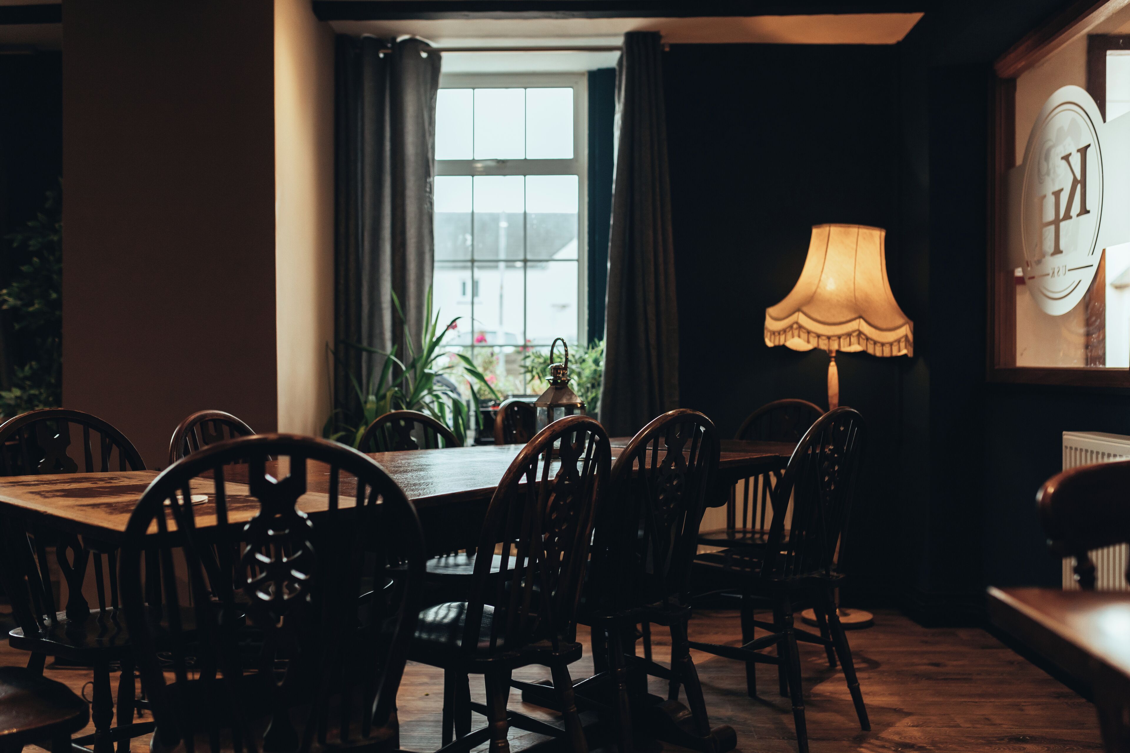 Un comedor con una mesa y sillas de madera, una lámpara y una ventana con cortinas.
